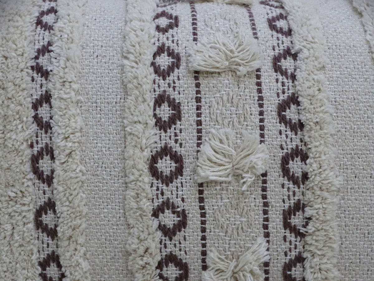 Close-up of handwoven cream-colored throw pillow with vertical brown geometric lines, textured fringe stripes, and three small horizontal fringe clusters.