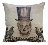 Light beige throw pillow with embroidered brown skull wearing a tall top hat, flanked by two brown birds perched on curling branches below.
