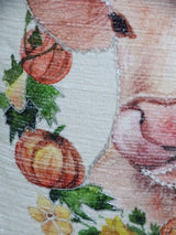 Close-up of a Thanksgiving-themed fabric showing stitched pumpkins, green leaves, yellow flowers, and part of a brown animal's face, possibly a deer, on textured material.