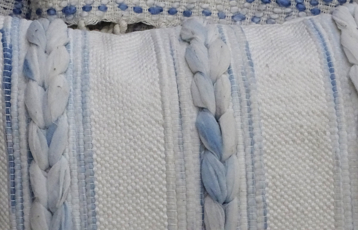 Close-up of a handwoven modern throw pillow with textured cream fabric featuring thick braided blue and off-white vertical stripes.