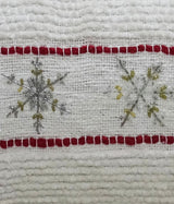 Close-up of white fabric with red horizontal stripes and silver and gold embroidered snowflakes on a textured holiday pillow