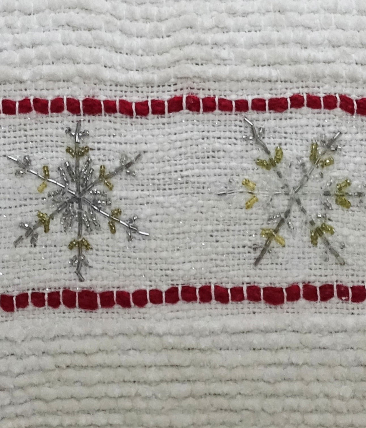 Close-up of white fabric with red horizontal stripes and silver and gold embroidered snowflakes on a textured holiday pillow
