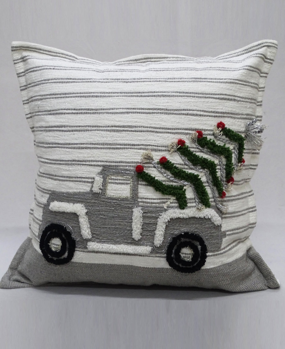 Square decorative pillow with light gray and white horizontal stripes, featuring a textured gray truck carrying a green Christmas tree with red ornaments and silver tinsel on the back.