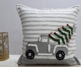 Square pillow with gray and white horizontal stripes, embroidered with a gray pickup truck carrying a green Christmas tree with red ornaments in the truck bed.