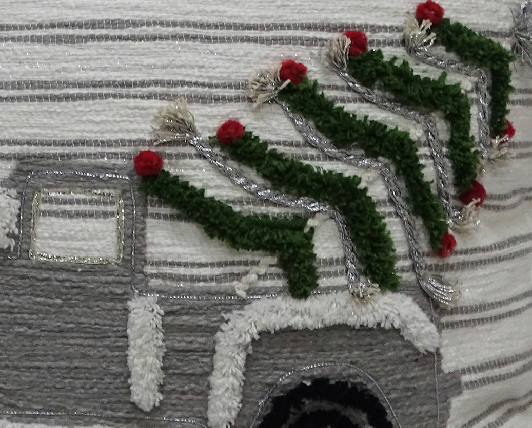 Close-up of a textured fabric showing green wreaths with red bows attached to a gray and white truck design outlined in silver thread on striped background.