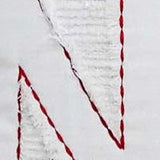 Close-up of a white Christmas pillow featuring a textured, glittery silver letter 'N' outlined with a red twisted rope trim.