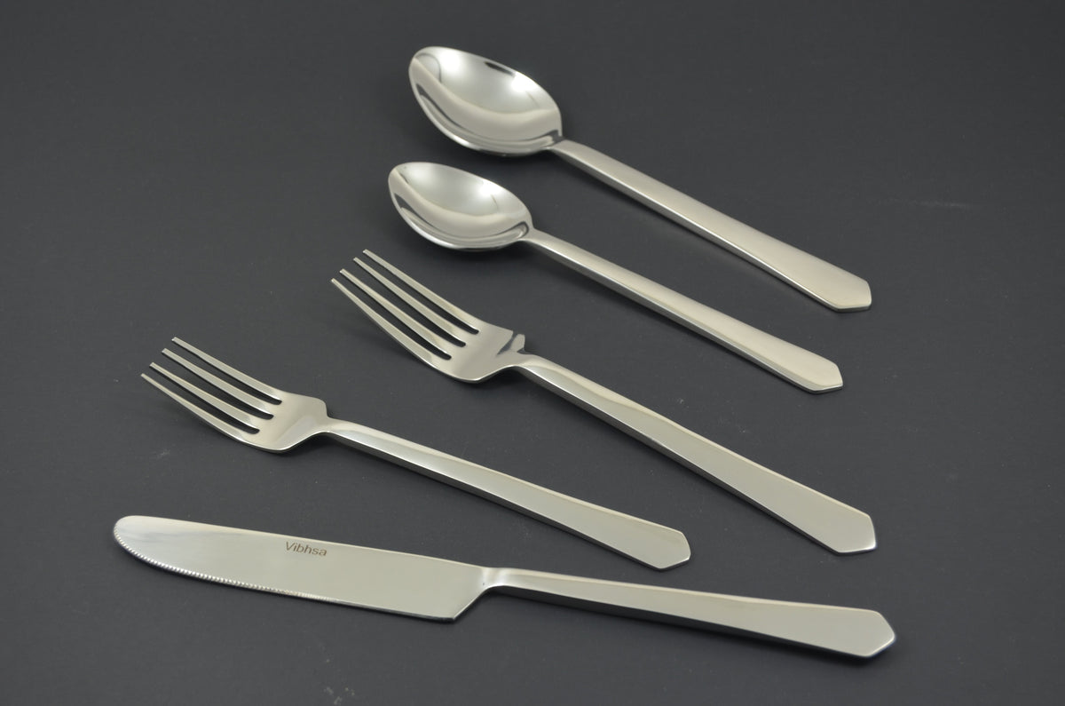 Set of five stainless steel flatware pieces including a serrated knife, two forks, and two spoons with straight, simple handles on a dark surface.