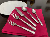 Five-piece silver stainless steel flatware set including two forks, one knife, one tablespoon, and one teaspoon arranged on a folded red napkin on a dark wood table.