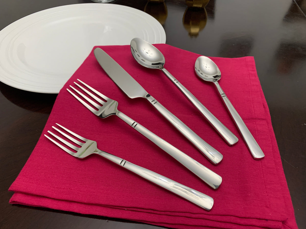 Five-piece silver stainless steel flatware set including two forks, one knife, one tablespoon, and one teaspoon arranged on a folded red napkin on a dark wood table.