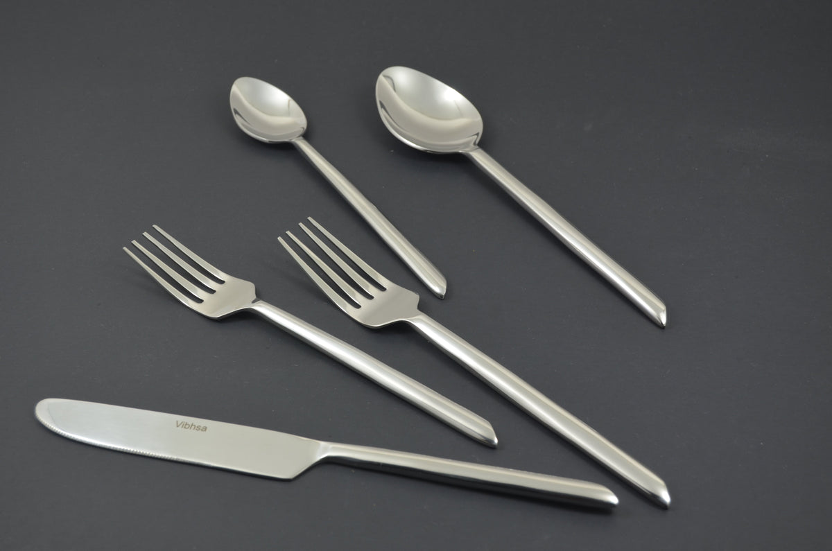 Silver stainless steel flatware including two forks, a knife, a tablespoon, and a teaspoon arranged on a dark gray surface.