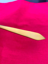 Close-up of a golden stainless steel utensil with a flat, rounded tip placed diagonally on a vibrant pink fabric background.