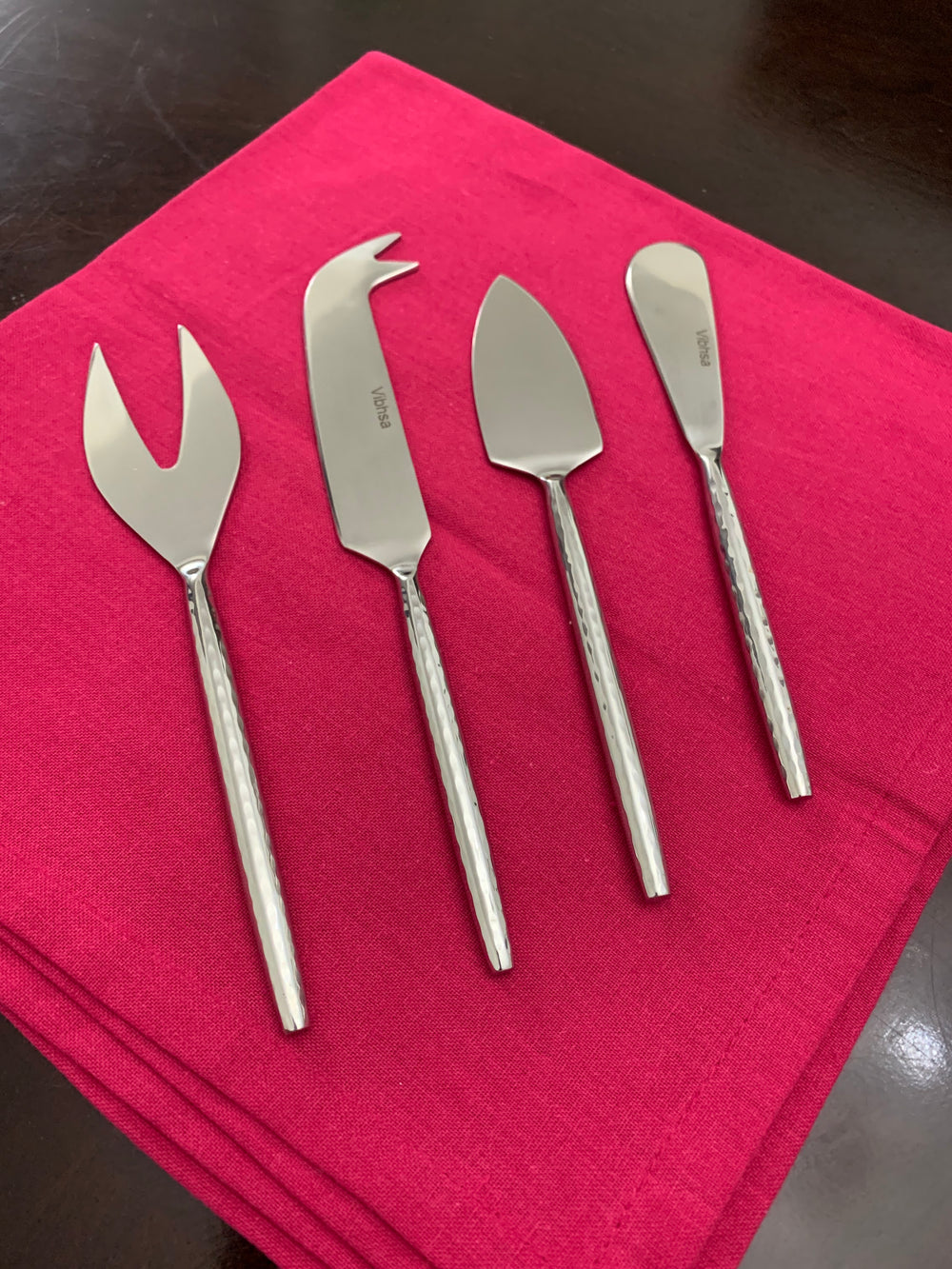 Set of four silver hand-forged cheese knives with hammered handles displayed on a wooden surface