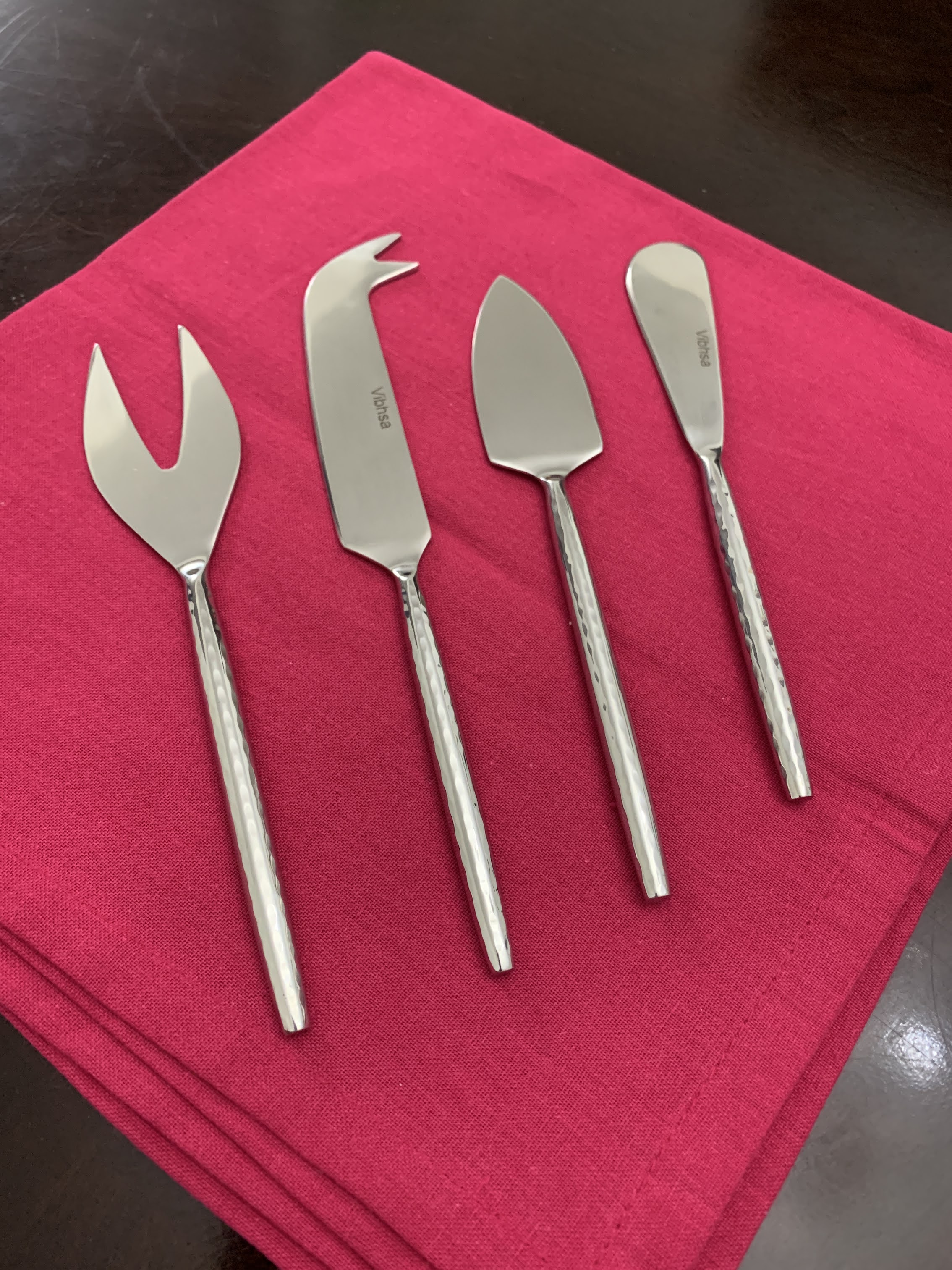 Set of four silver hand-forged cheese knives with hammered handles displayed on a wooden surface