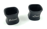 Two black napkin rings with curved sides and silver script text reading 'Believe' and 'Love' on a white background.