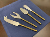 Set of four stainless steel cheese knives with twisted golden handles and distinct blade shapes, arranged on a blue cloth on a wooden surface.