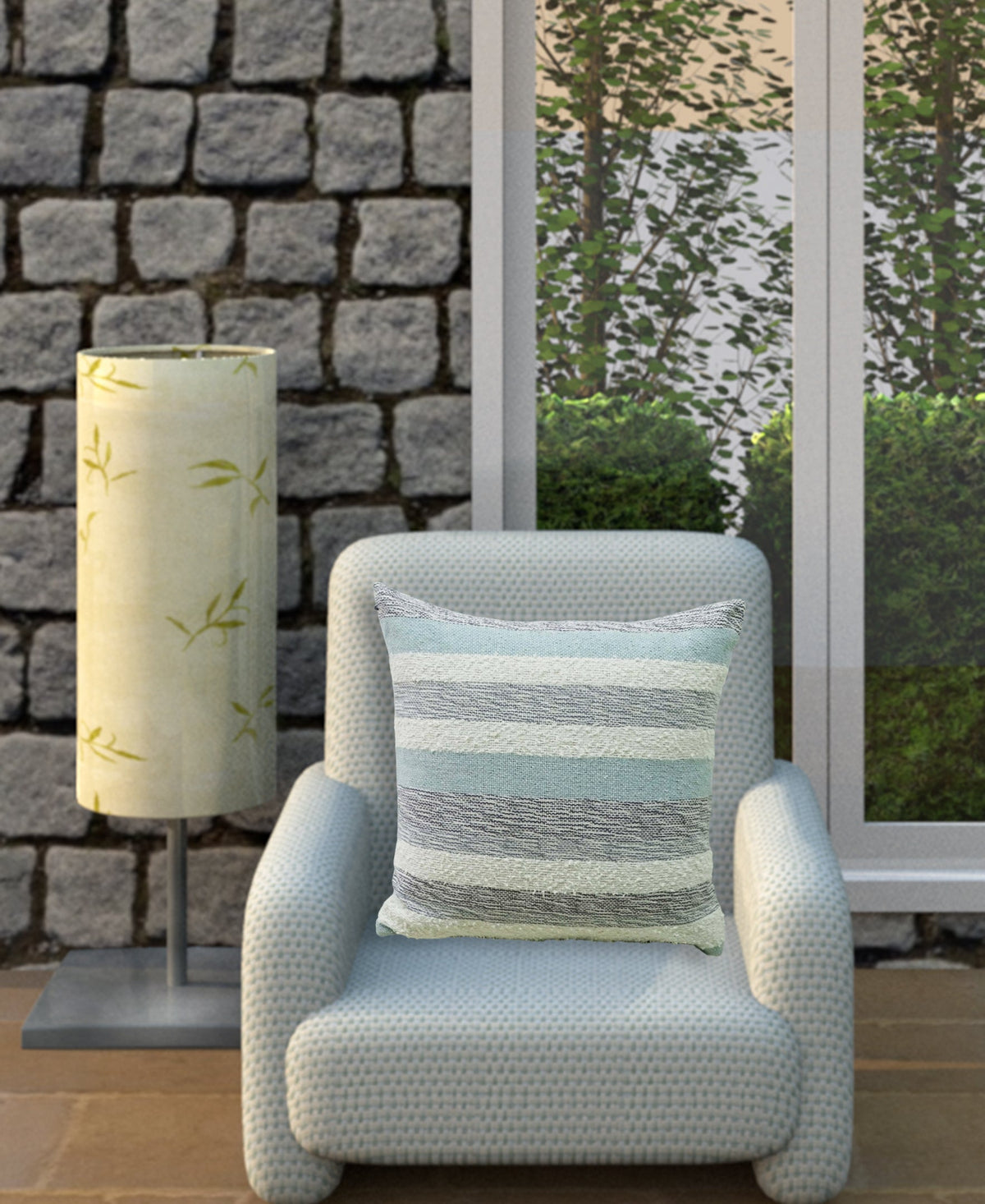 Light blue textured armchair with a striped decorative pillow in shades of blue and gray, positioned in front of a window and beside a cylindrical lamp with leaf patterns.