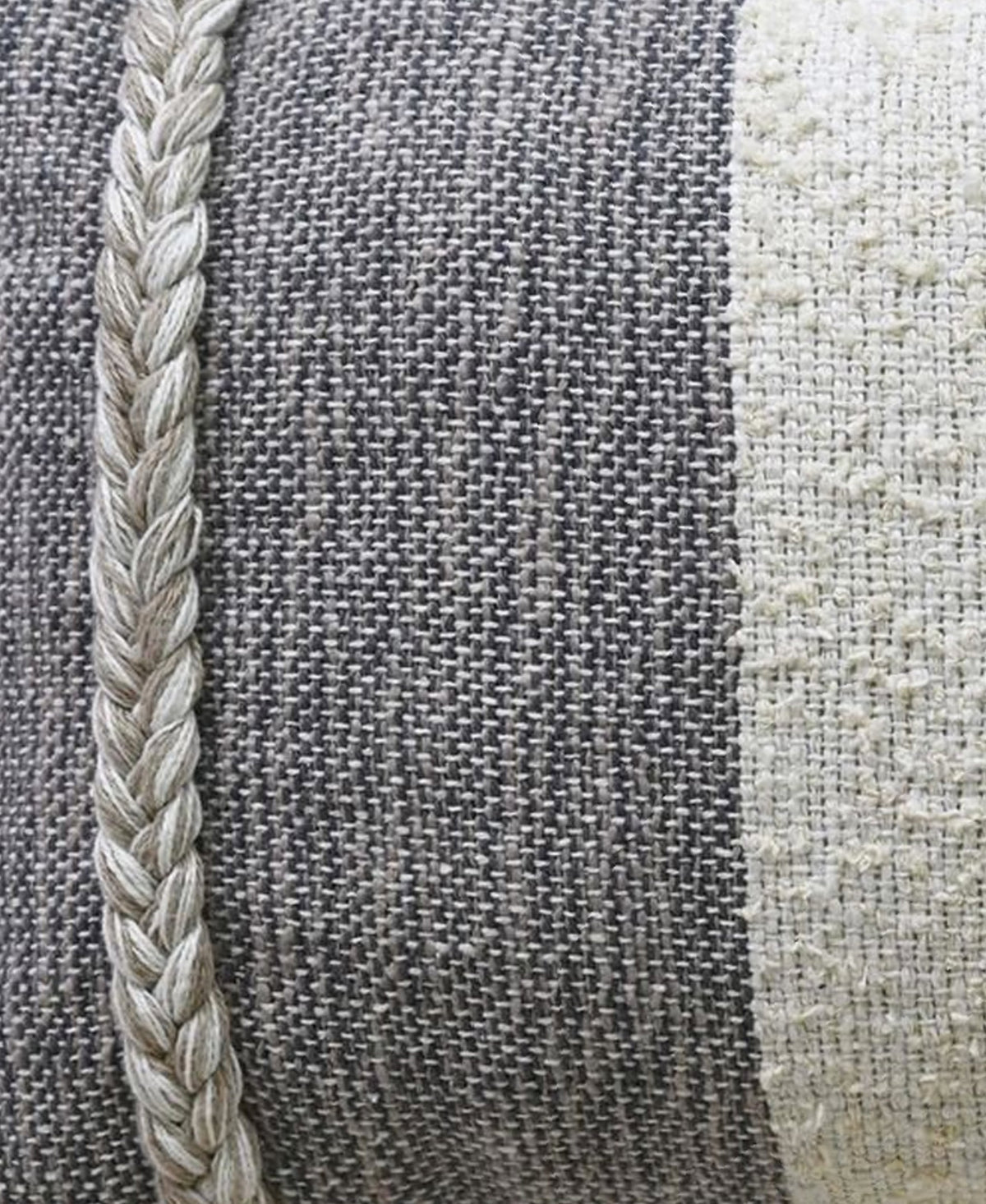 Close-up of a woven throw pillow featuring a central dark gray textured fabric panel bordered by a thick cream-colored braided trim and a cream woven stripe.