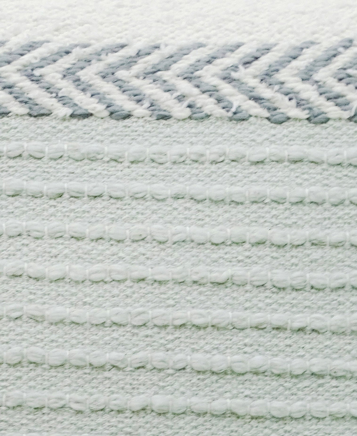 Close-up of a handloom woven pillow showing white and light gray horizontal stripes with textured, raised thread patterns and a zigzag chevron detail at the top