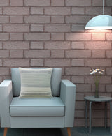 Light gray armchair with a cream-colored woven pillow featuring horizontal stripes and chevron patterns, set against a muted brick wall with a side table and a hanging lamp.