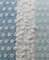 Close-up of handwoven pillow fabric showing blue and teal diagonal patterned stripes with a central white buttknot edging featuring textured loops.
