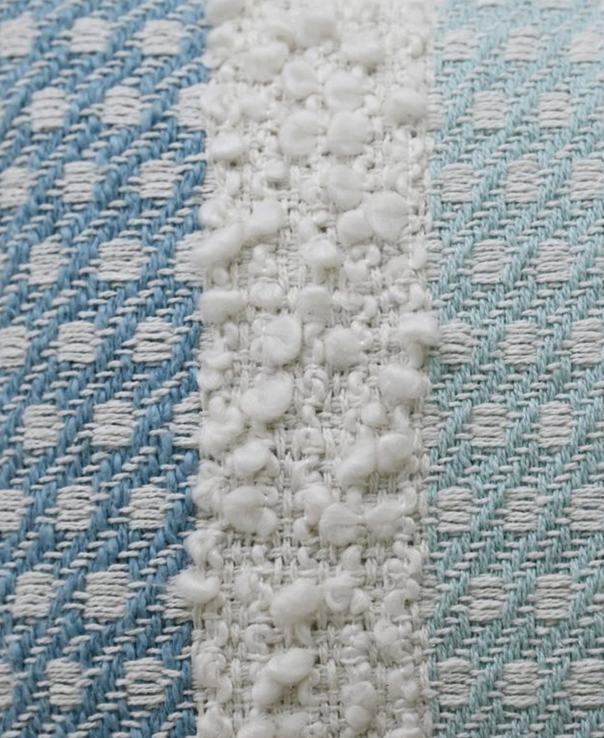 Close-up of handwoven pillow fabric showing blue and teal diagonal patterned stripes with a central white buttknot edging featuring textured loops.