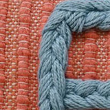 Close-up of handwoven braid couching technique on coral fabric with tightly woven vertical threads and light blue braided yarn detail.