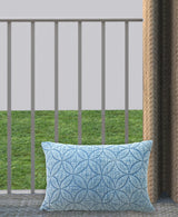Rectangular decorative pillow with a blue textured quilted pattern of overlapping circles on a light blue background, placed upright on a balcony railing.