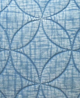 Close-up of a light blue decorative pillow with a textured quilted pattern forming overlapping circular shapes and subtle linear texture inside each shape.