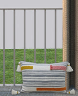 Rectangular handwoven decorative pillow with blue and cream stripes, accented by mustard yellow, coral pink, and burnt orange embroidered braids, finished with cream tassels on corners.