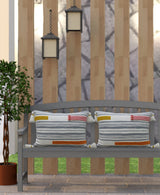 Two rectangular handwoven pillows with horizontal gray stripes and small colorful braid accents in orange, mustard, and pink, placed on a gray wooden bench outdoors.