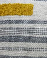 Close-up of a handwoven pillow fabric with textured mustard yellow embroidery above horizontal stripes in various gray and white woven patterns.