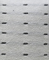 Close-up of a light gray handwoven pillow fabric with evenly spaced small black oval accents creating a simple dotted pattern.