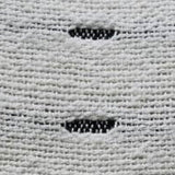 Close-up of a light gray handwoven pillow fabric featuring small, evenly spaced black oval patterns woven into the texture.