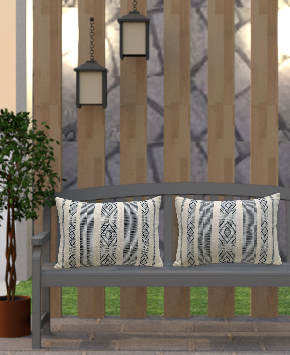 Rectangular throw pillows with blue and cream geometric jacquard patterns placed on a gray painted wooden bench outdoors against a vertical wood panel fence.