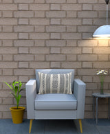 Rectangular jacquard woven throw pillow with black geometric diamond patterns and beige stripes, placed on a light gray armchair against a tan brick wall.