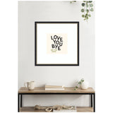 Square black-framed wall art with quirky black typography reading 'LOVE YOU BYE' and smaller text 'SEE YOU SOON' on a soft beige background, hanging above a wood and metal table.