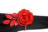 Bright red metal napkin ring shaped like a detailed rose with leaves, displayed on a black cloth napkin against a white background.