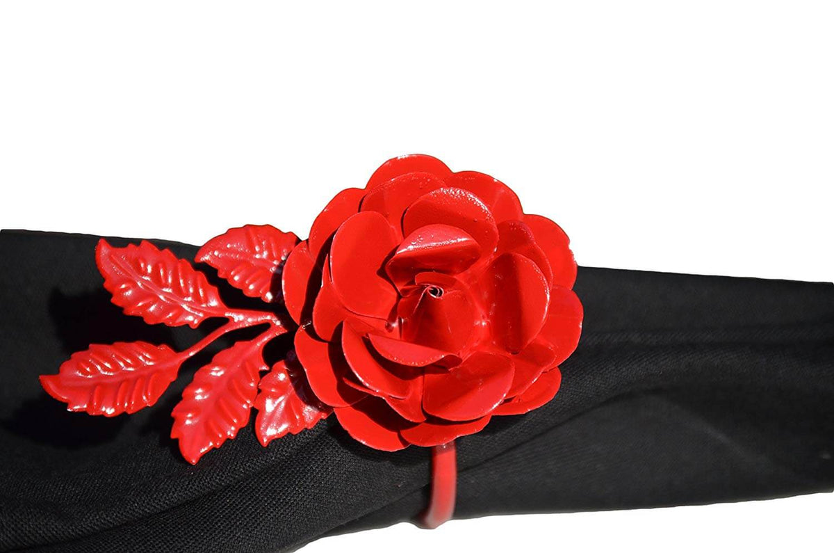 Bright red metal napkin ring shaped like a detailed rose with leaves, displayed on a black cloth napkin against a white background.