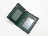 Open dark green leather pass case with two transparent ID card windows and a small metal snap button on the right side.