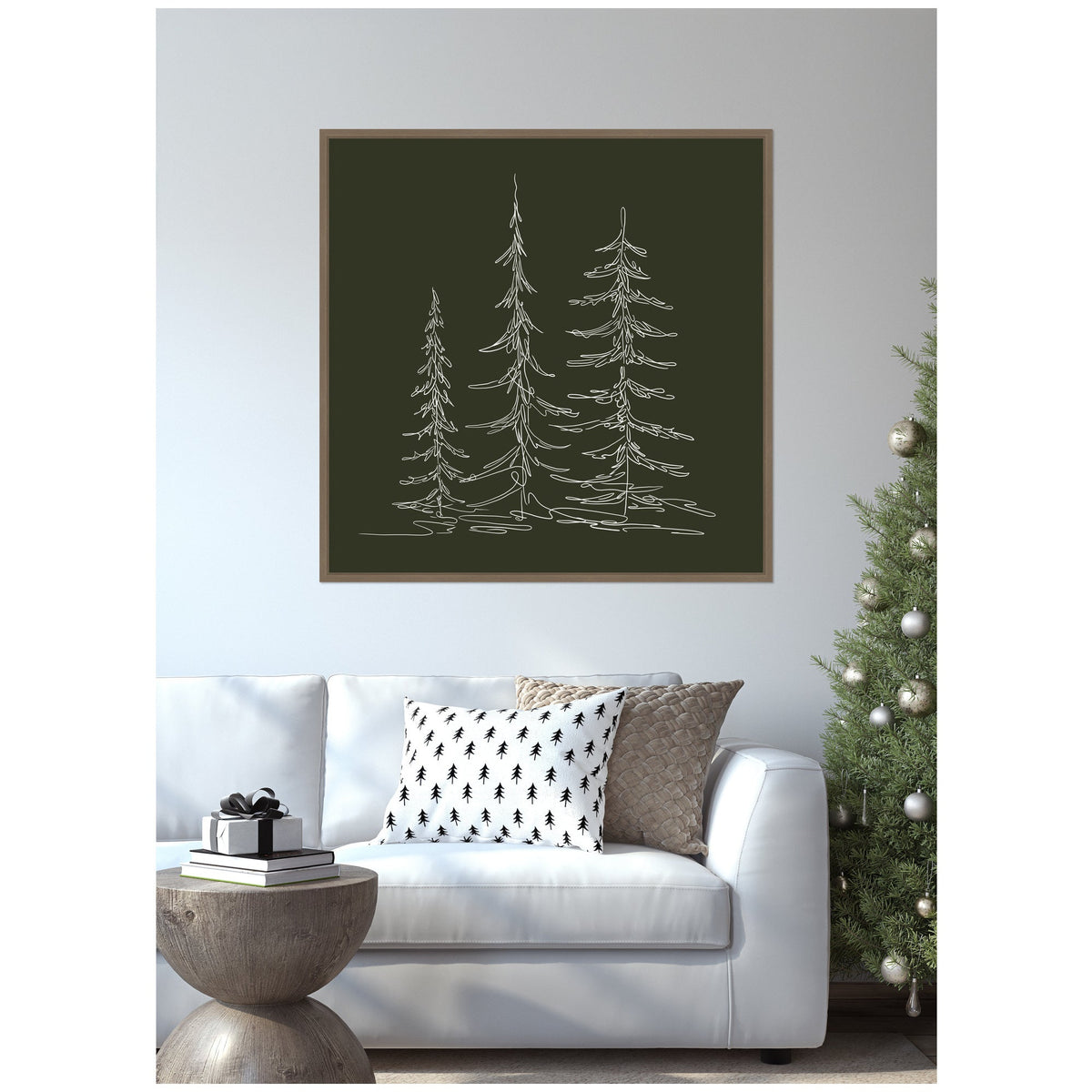 Framed minimalist canvas sketch of three white evergreen trees on dark green background above white sofa with patterned cushions and modern round wooden side table.
