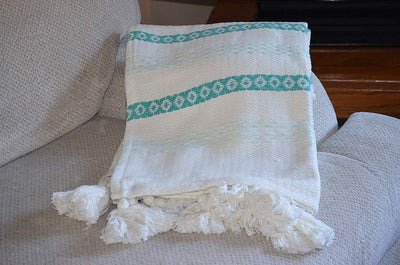 Turquoise and white hand loom woven throw with chunky tassels draped on a couch