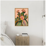 Framed painting of green and pink cacti with blooming flowers on a peach background, hanging above a rustic wooden bedside table with a cup and books.