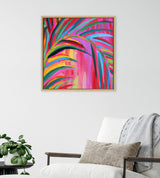Abstract painting with bold, colorful arched brushstrokes in pink, red, purple, yellow, and teal, framed in light wood, hanging on a white wall above a white armchair.
