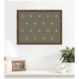 Rectangular wooden-framed artwork with repeating white botanical block prints on a muted green background, hanging above a white shelf with lamp, photo frame, and potted plant.