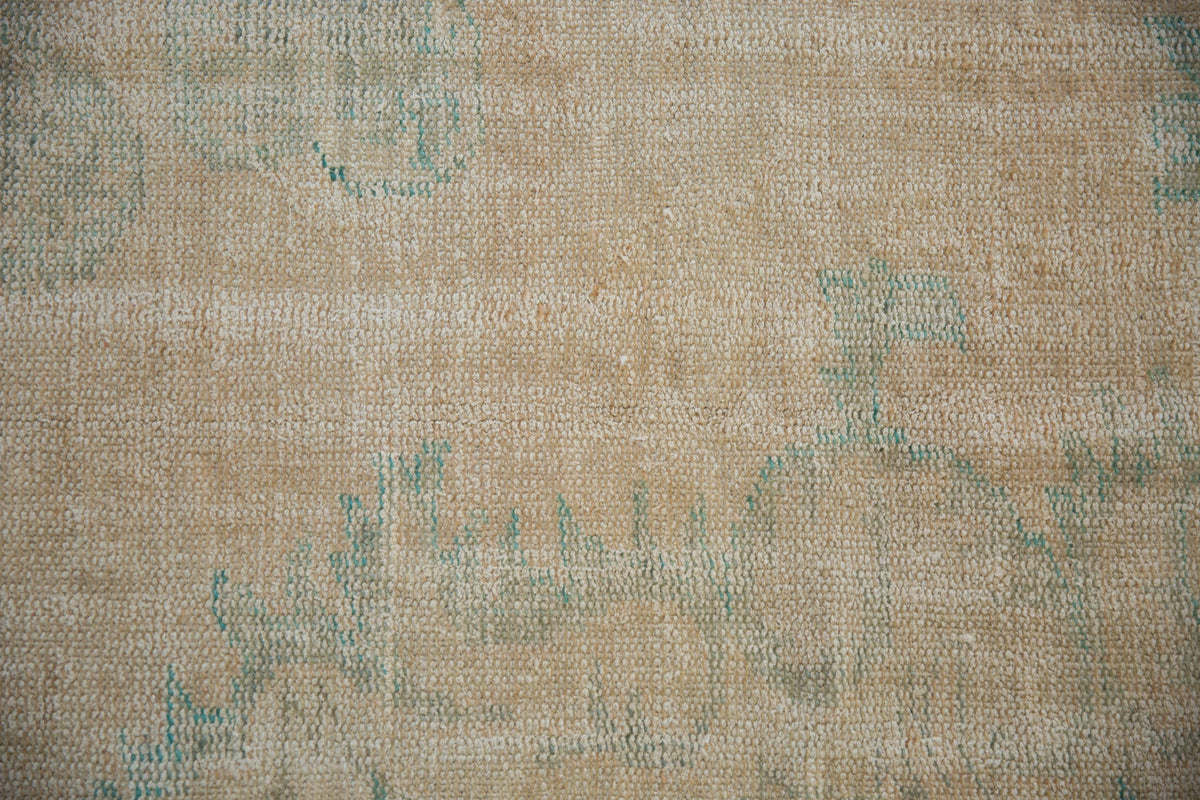 Close-up of a 6.5x10 vintage distressed Oushak carpet with muted beige and light blue floral patterns and a textured woven surface.