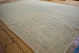 Muted vintage Oushak carpet in soft beige with faded light blue and green floral patterns on wooden floorboards, showing subtle texture and wear.