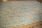 Faded vintage Oushak carpet in soft beige with distressed teal geometric and floral patterns on a wooden floor.