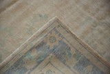 Close-up of a vintage distressed Oushak carpet corner with muted blue, beige, and green floral and geometric patterns on a faded beige background.