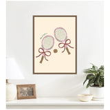 Framed wall art depicting two pastel pink tennis rackets with bows tied around their handles and a tennis ball between them on a cream background.