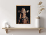 Framed portrait of a brown horse wearing a tan cowboy hat and saddle, set against a black background, displayed above a wooden shelf with decorative vases.